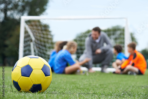 Coach And Team Discussing Soccer Tactics With Ball In Foregroun