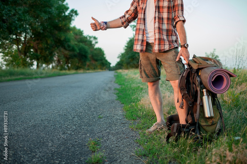 Young smilimg caucasian tourist hitchhiking along a road.