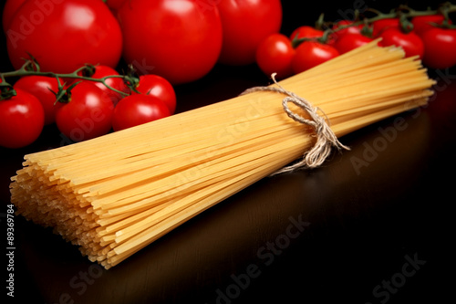 Long pasta raw isolated on black table with tomatoes