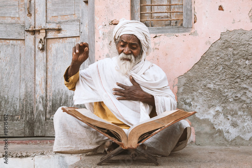 Close up of an old indian sadhu (saint) sitting and reading sacred texts near the temple. 