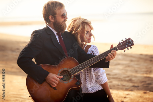 guitarist and blonde girl standing on sandy beach