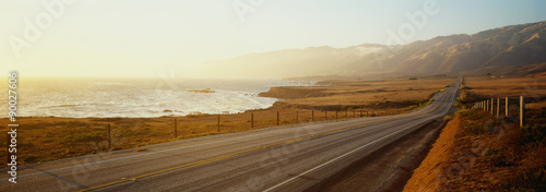 Jest to trasa 1 znana również jako autostrada Pacific Coast. Droga znajduje się nad oceanem, w oddali góry. Droga biegnie w nieskończoność w zachód słońca.