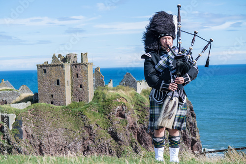 Traditional scottish bagpiper in full dress code at Dunnottar Castle in Stonehaven