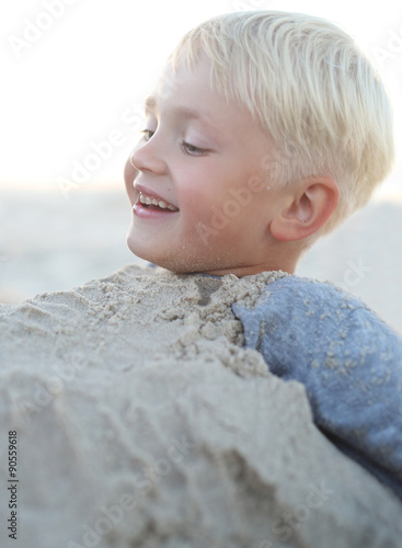 Zabawa na plaży.Wesoły chłopiec bawi się w piasku na plaży
