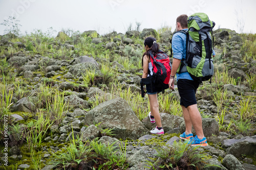 Mixed race couple go trekking together, walking on an uphill, n