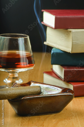 Drink w kieliszku, zapalone cygaro i książki