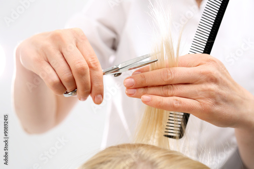Podcinanie rozdwojonych końcówek włosów.Fryzjer strzyże kobietę w salonie fryzjerskim 