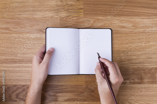 Mano con pluma escribiendo en libreta en blanco