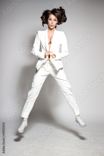 Awesome caucasian attractive joyful happy sexy dance model is jumping in studio wearing white suit on gray background