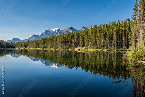 Snow capped peaks reflect on Herbert Lake in Banff National Park