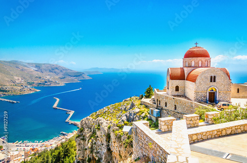 Daleki kościół z czerwonym zadaszeniem na falezie, Grecja