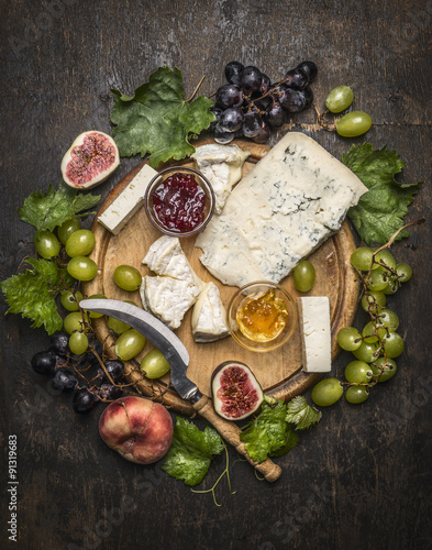 cheese plate with gorgonzola and Camembert cheese with Knife for cheese white and dark grapes, honey and jam on a wooden cutting board on a dark rustic background top view close up