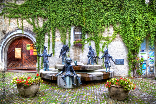 Ein wunderschöner Vorplatz in Lindau am Bodensee im Süden Deutschlands mit Statuen, einem Brunnen und einem alten Haus mit grünem Efeu