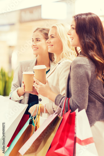 young women with shopping bags and coffee in mall