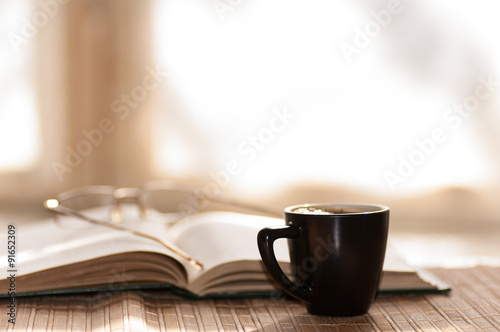 cup of coffee glasses rest on the open book against the window i