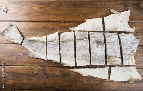 Corte tradicional en porciones del bacalao salado, pescado seco conservado en sal sobre fondo de madera