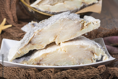 Lomos de bacalao salado cortados, pescado seco conservado en sal sobre fondo de redes de pesca