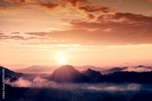 Misty dreamy landscape with autumn fog between hills and orange sky within early sunrise