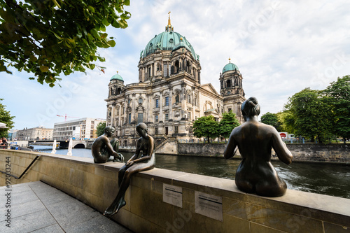 3 statues sit at the riverside. In the background is the Berliner Dom.