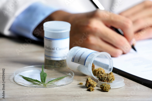 Doctor writing on prescription blank and bottle with medical cannabis on table close up