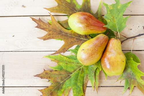 Red pears and autumn yellow maple leaves on a wooden table, close up, selective focus