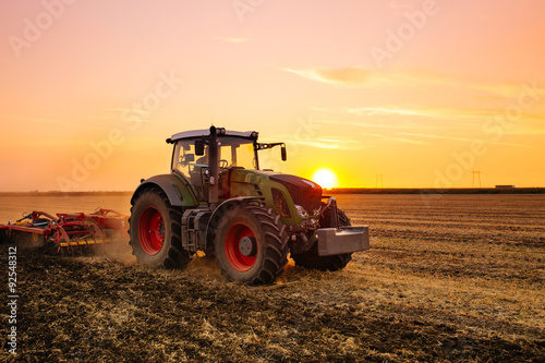 Tractor on the barley field by sunset.