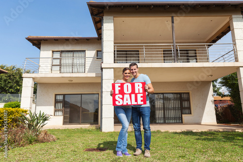 couple holding for sale sign in front of house