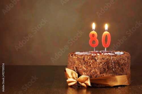 Birthday chocolate cake with burning candles as a number eighty on brown background