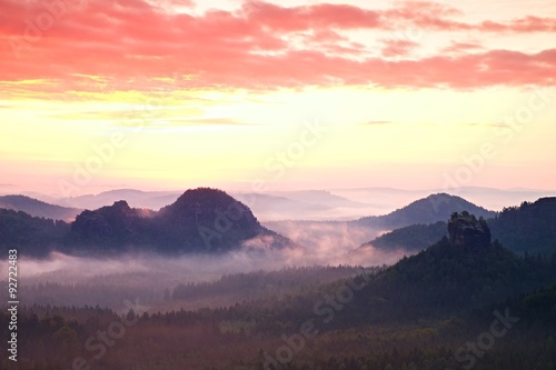 Red daybreak. Misty daybreak in a beautiful hills. Peaks of hills are sticking out from foggy background, the fog is red and orange due to Sun rays.