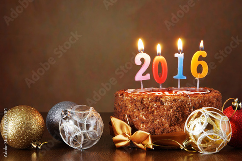 New Year 2016 still life. Chocolate cake and decorative tree balls with burning candles on brown background