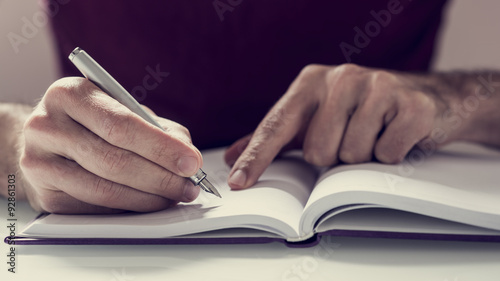 Male student writing notes with fountain pen in his notebook