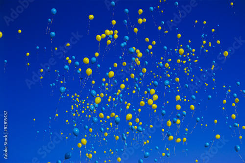 yellow and blue balloons soar into the cloudless sky