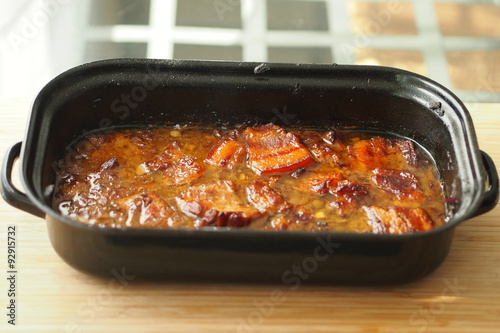 Baked pork belly with a sauce in a black roasting pan on a wooden table. Traditional specialty form the Czech Republic called "moravsky vrabec".