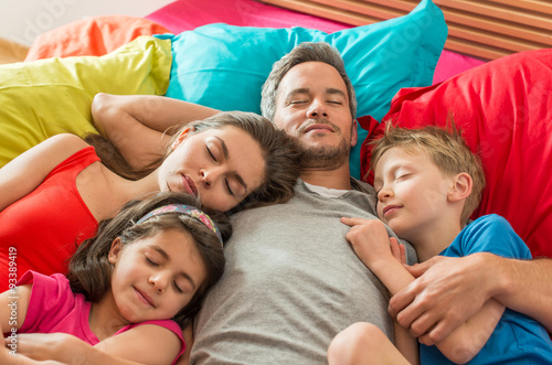 A family is taking a nap all together in a colorful bed 