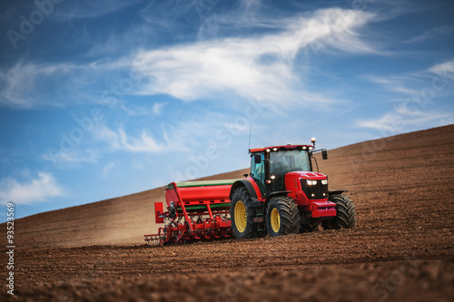 Farmer with tractor seeding crops at field