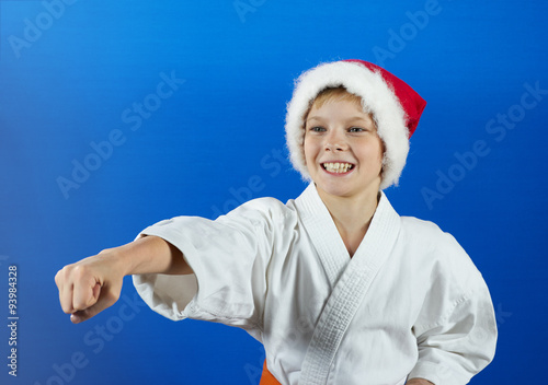 Boy in Santa hat make a karate punch on the blue background