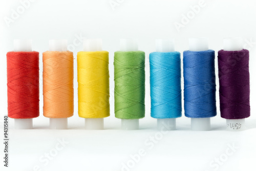 Ряд разноцветных швейных ниток на катушке.