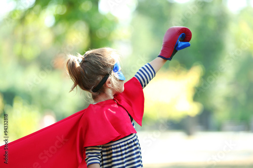 Cute little girl dressed as superhero in boxing gloves at the park