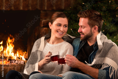 Couple relaxing with glass of mulled wine at fireplace