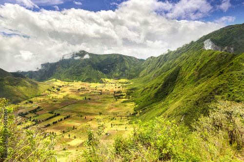A lush green crater of Pululahua in Ecuador, South America. Farmers work the fertile land with Quito city in the background.