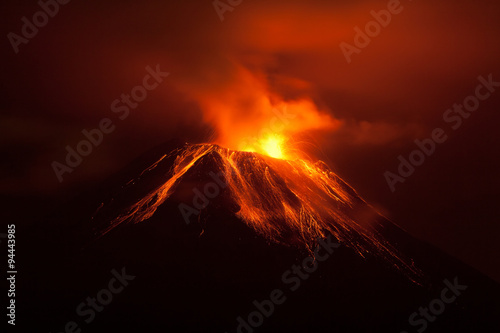 A breathtaking scene of an active volcano in Ecuador erupting at night, spewing lava and magma into the dark sky over rocky mountains.