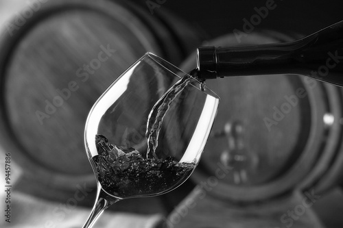 Pouring red wine from bottle into glass, black and white retro stylization
