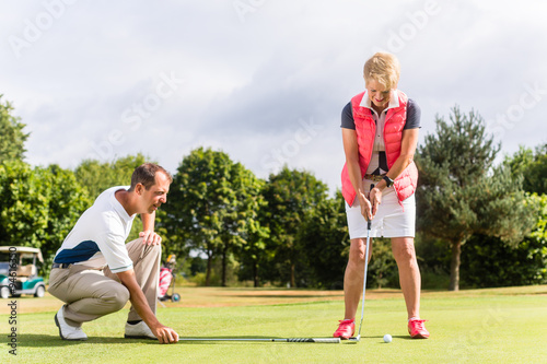 Seniorin und Golflehrer üben Golf auf dem Platz