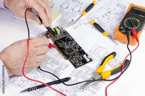 Electronics engineer testing a computer PCI card with a multi meter