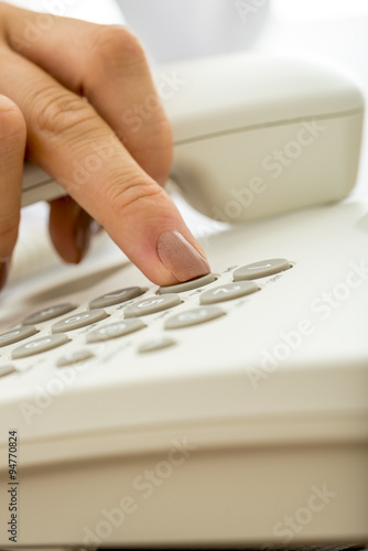 Closeup of female hand dialing a telephone number on a white lan
