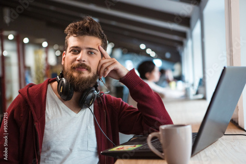 Young confident guy working in office using headset and laptop