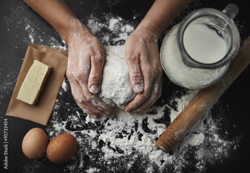 Woman hands kneading dough on the black board with eggs, milk, butter and flour. Healthy breakfast preparation concept. 