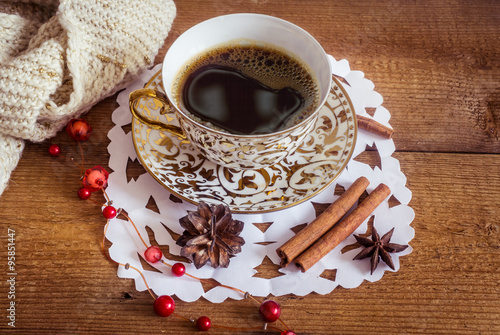 Photo of glowing white and golden cup with tasty coffee, Christmastime table setting, tea mug on brown wooden background, snowflake decoration, New Year ornament, Christmas home decor with warm scarf 