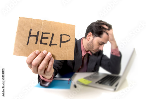 businessman in suit and tie sitting at office desk working on computer laptop asking for help holding cardboard sign