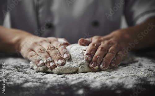 Close-up of woman baker hands kneading the dough on black board with flour powder. Concept of baking and patisserie. 